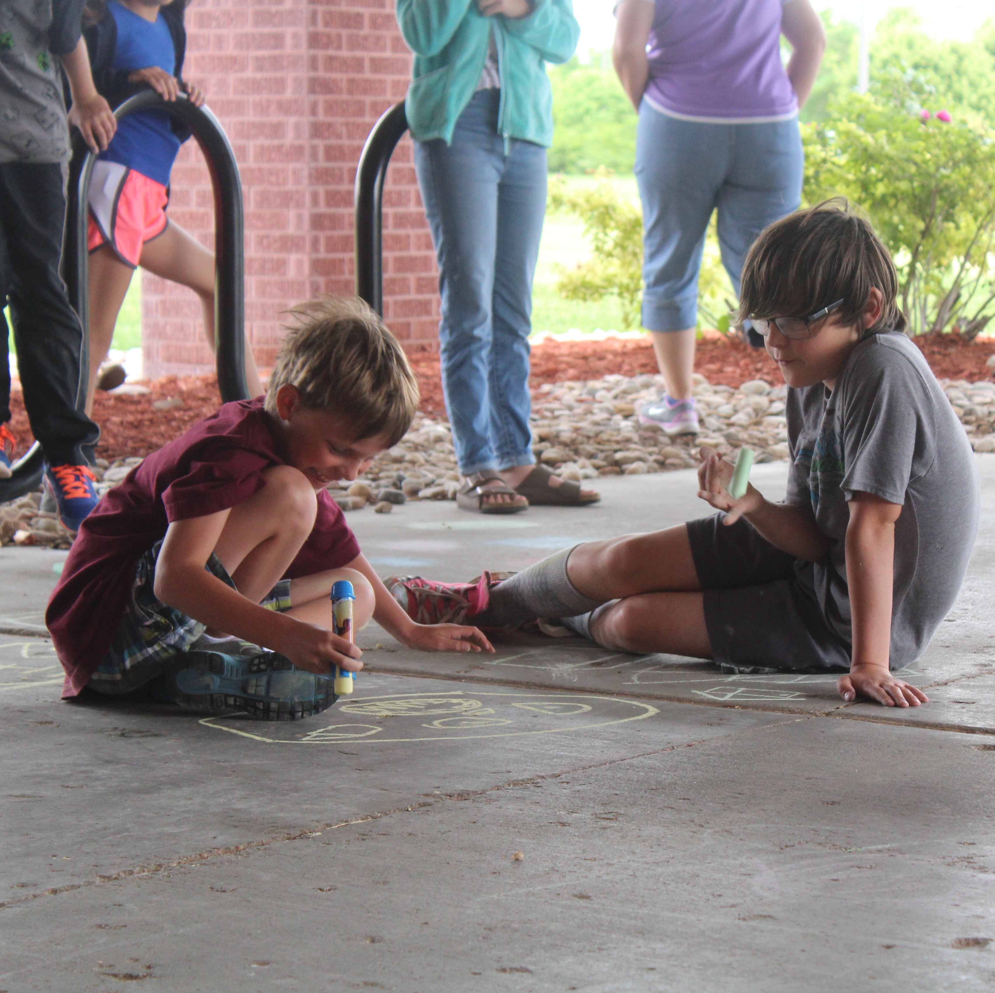 BCE kids camp photo of children drawing with chalk on concrete. 